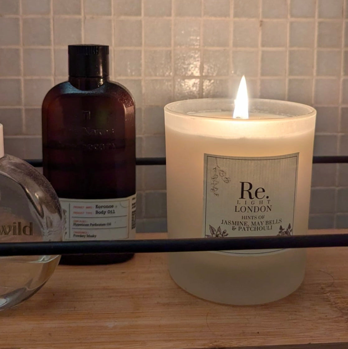 Re. Candle with a label on a wooden surface next to a bottle, against a tiled wall background.