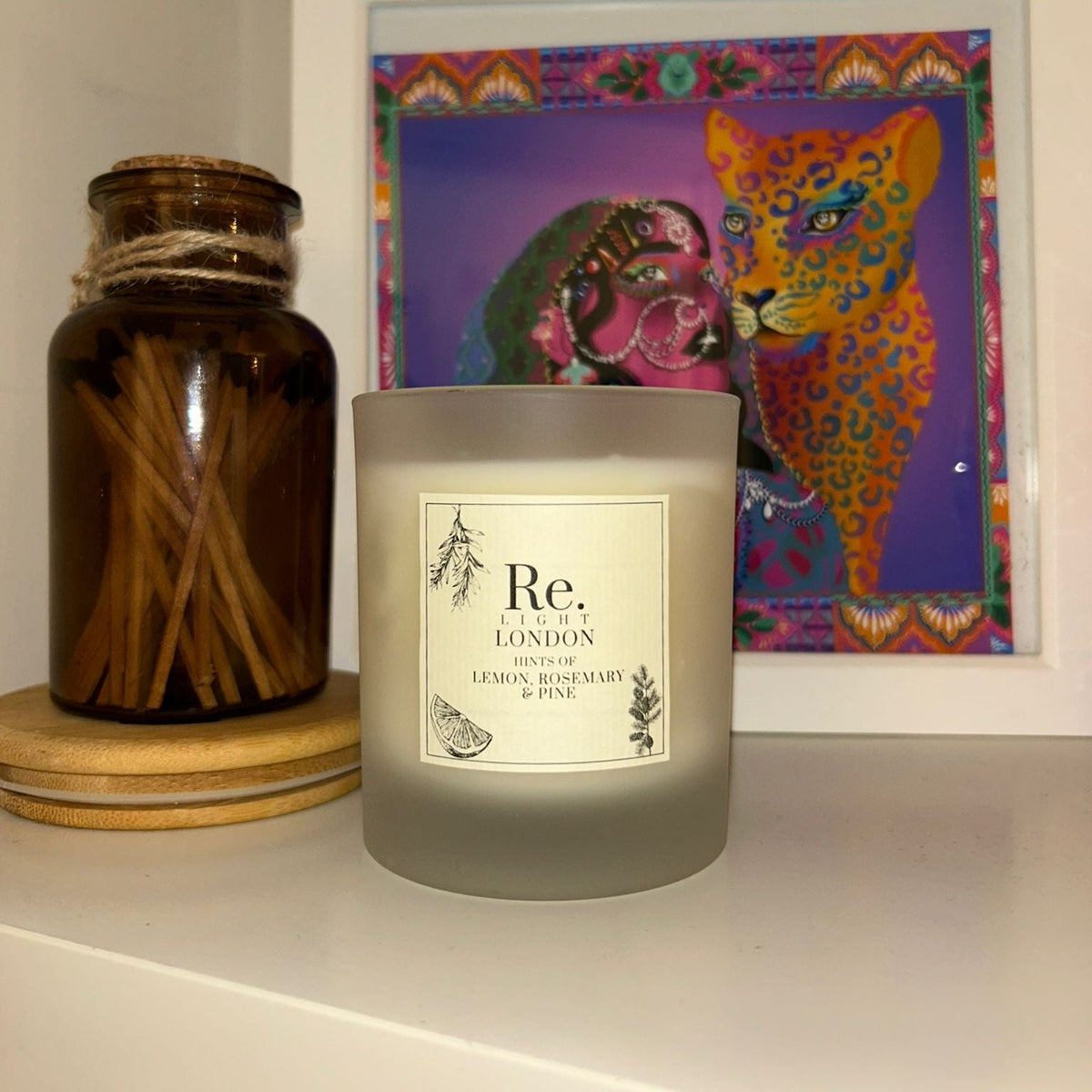 Candle labeled 'Re' on a shelf with a colorful framed picture of two animals in the background.