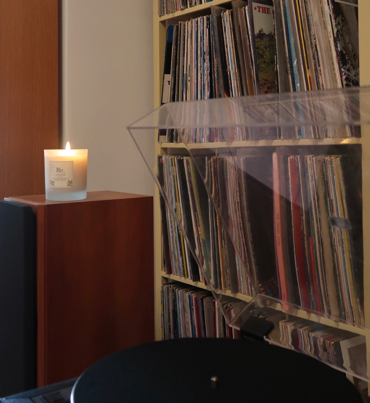 Record player with vinyl records on a shelf and a lit Jazz candle on a stand.