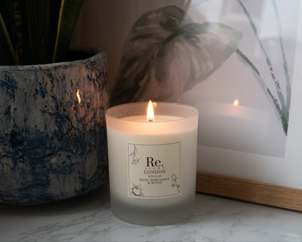 Rosie candle with 'Re' branding on a surface next to a plant and framed picture